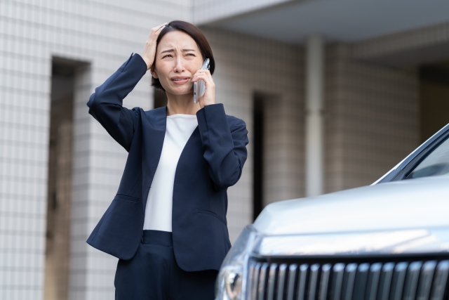車の近くで困った顔をして電話するビジネスウーマン