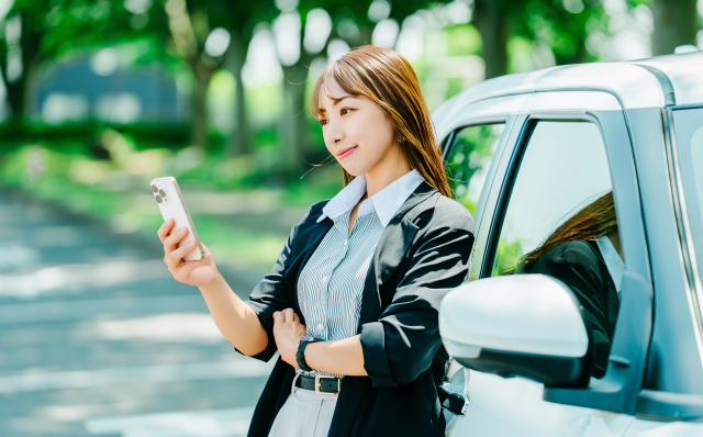 車にもたれてスマホを触る女性